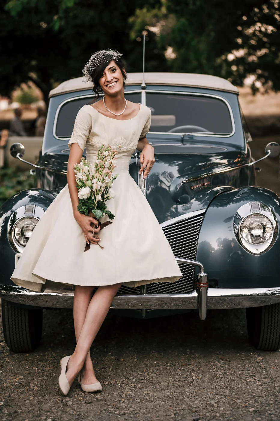 Bride is all smiles as she poses in front of a vintage car at her wedding