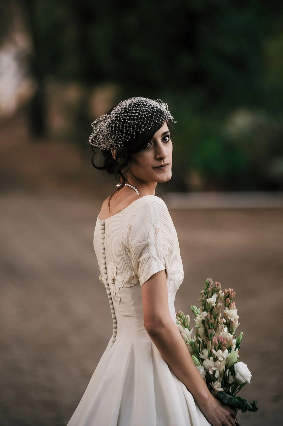 Bride looks back at her groom lovingly as she poses with her bouquet at a vintage themed wedding in temecula