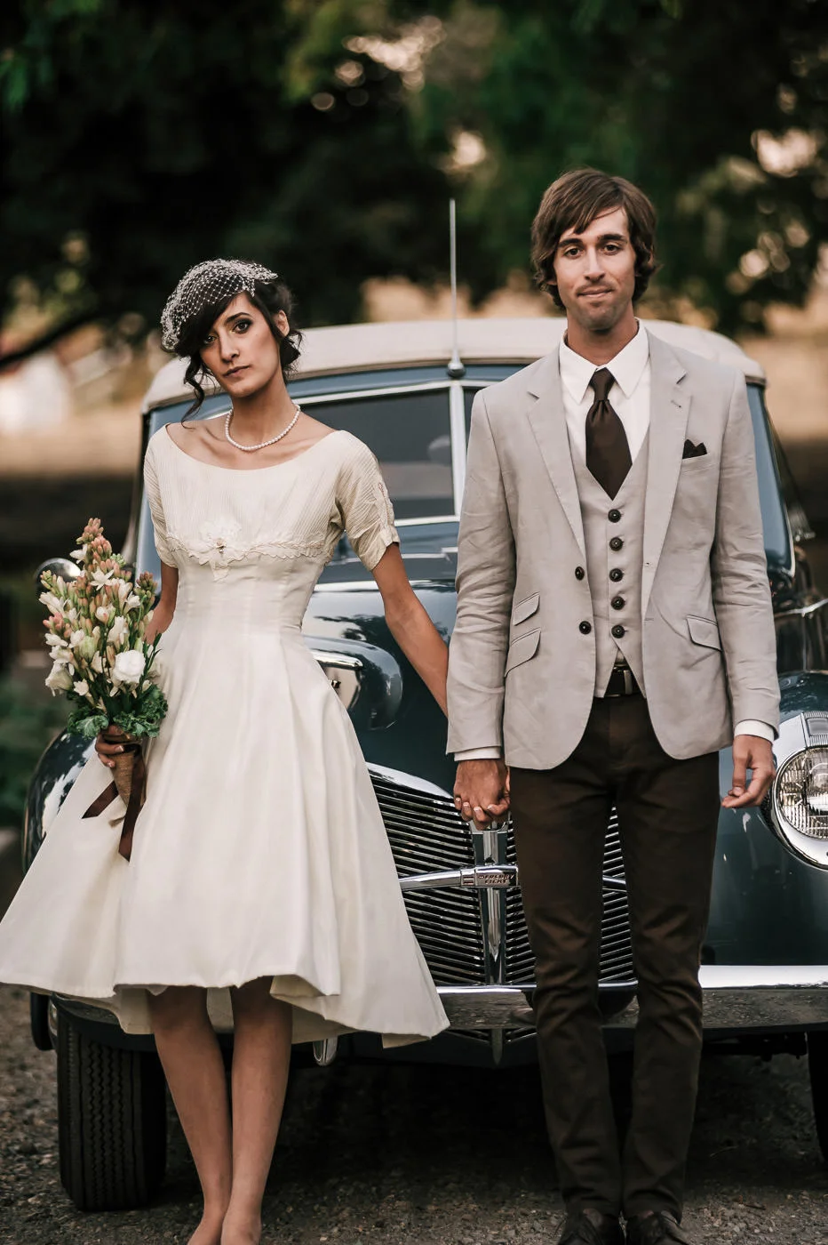 Bride and groom put on a serious face as the pose in front of a classic convertible