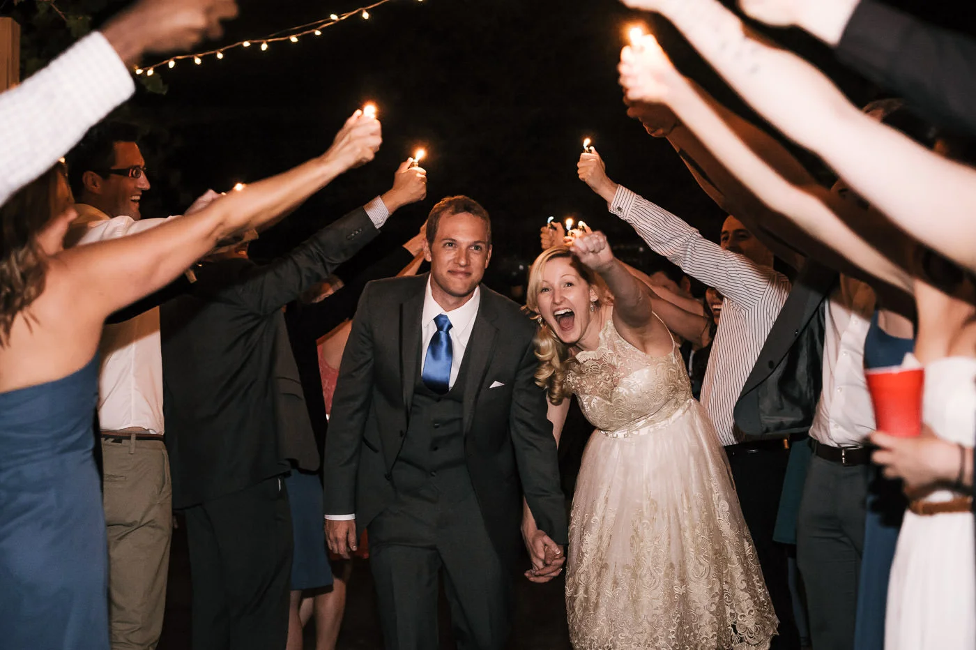 Bride and groom make their grand exit through a tunnel of their guests holding lighters on high