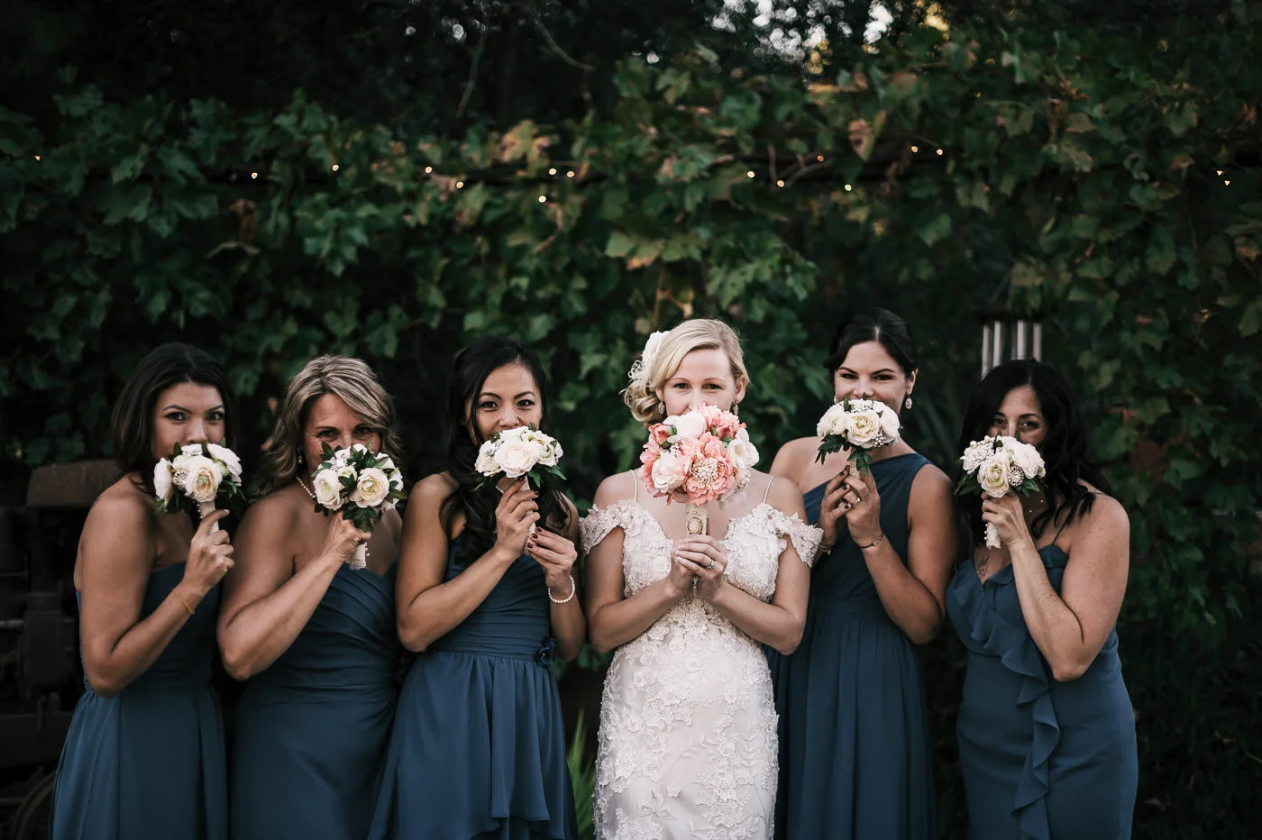 bride and her bridesmaids playfully hide behind their flower bouquets