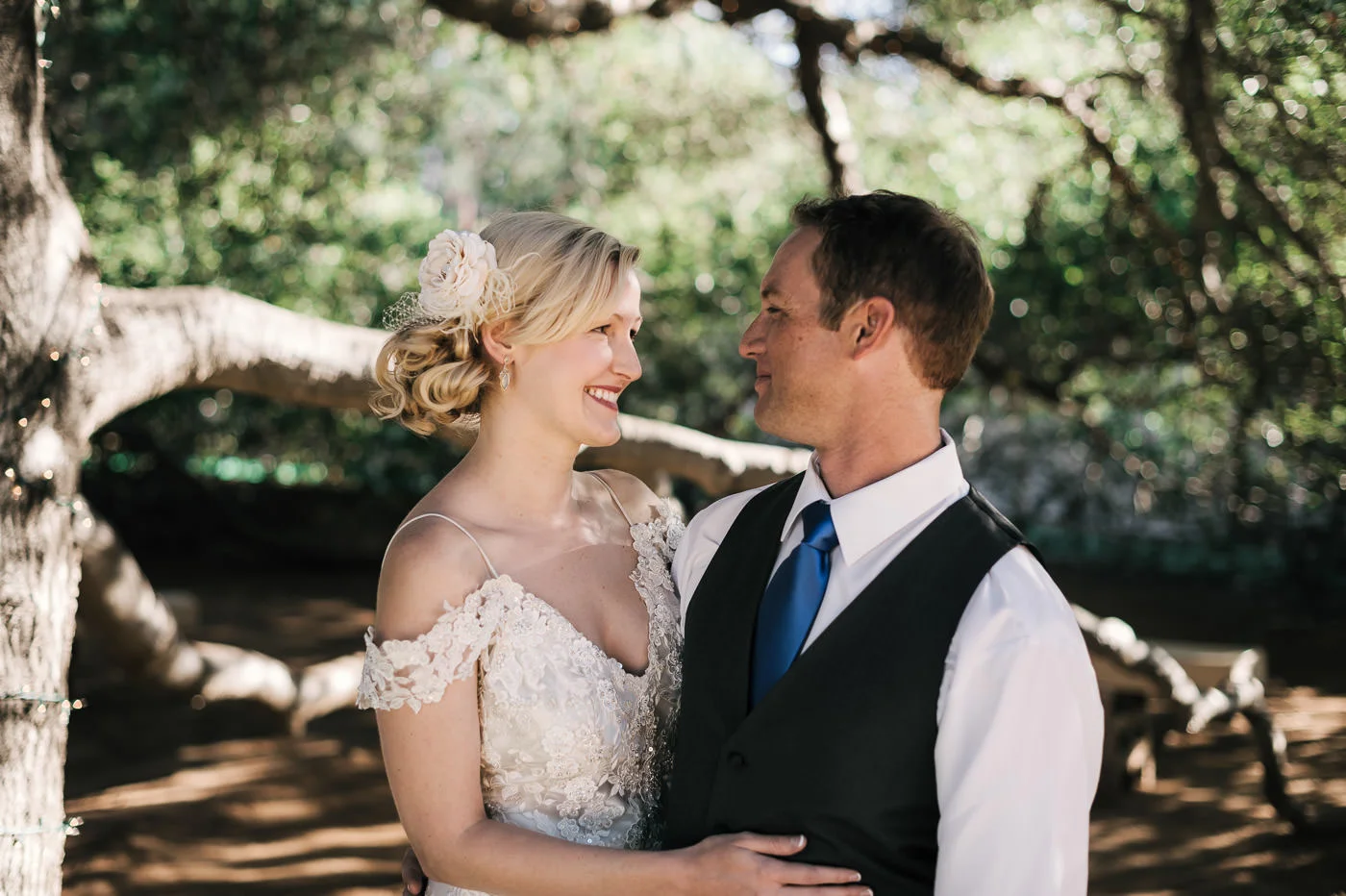 bride and groom enjoy the shade of an old oak tree as they smile at each other after an intimate first look