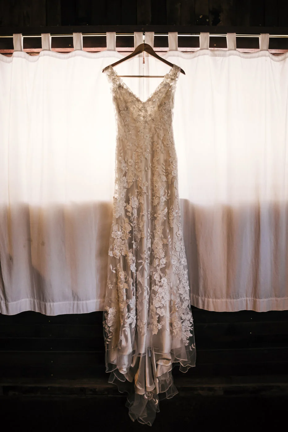 brides beautiful dress for the wedding ceremony backlit by window light as it hangs in the dressing room.