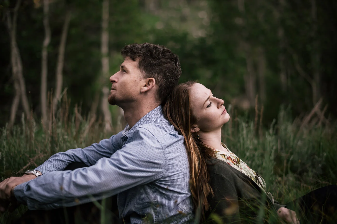 couple sits in a meadow back to back and enjoys a quiet moment alone during their engagement session in seqouia national park