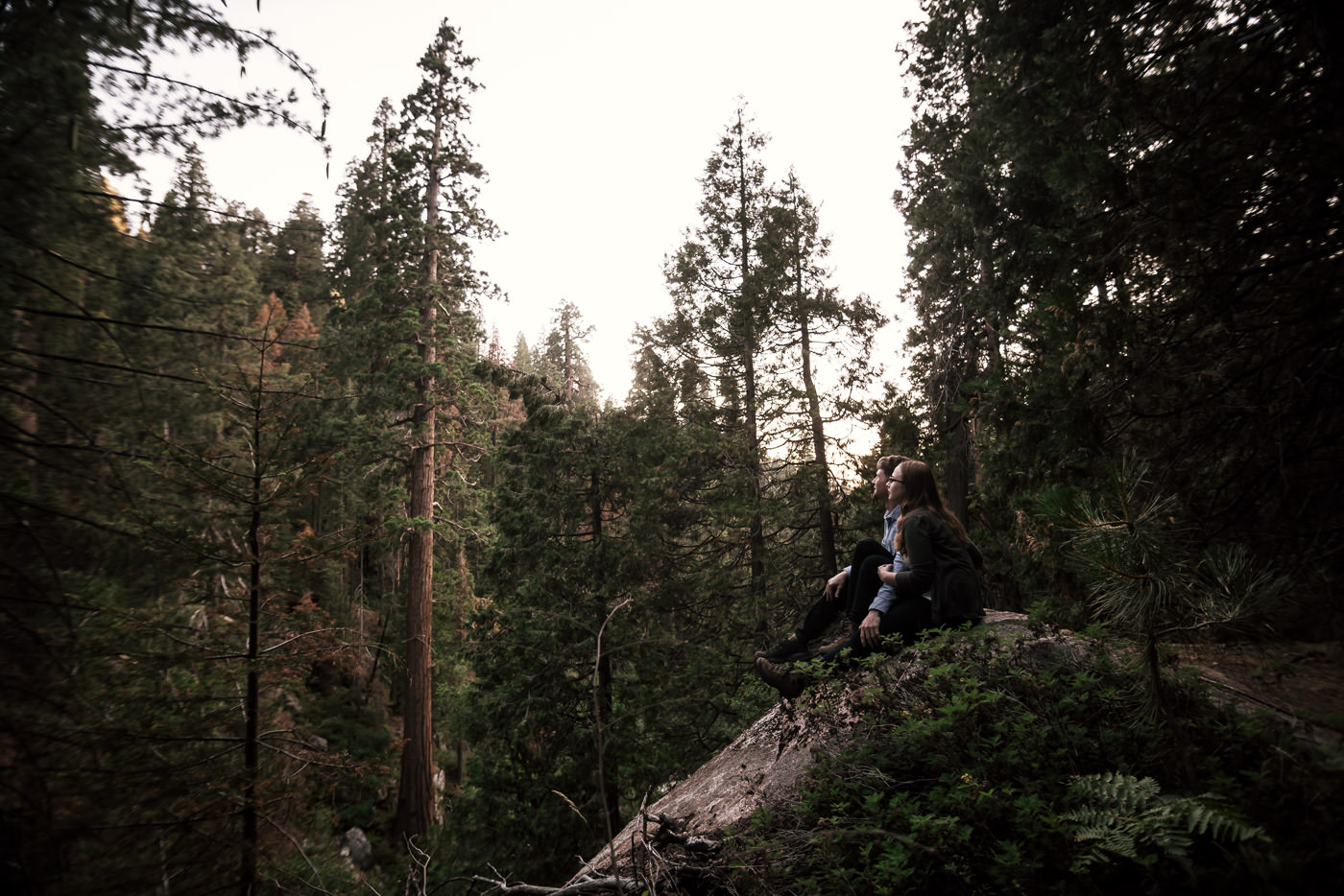 two lovebirds sit on a rock overlook and take in the sights of Sequoia national park after their intimate engagement session i nthe woods