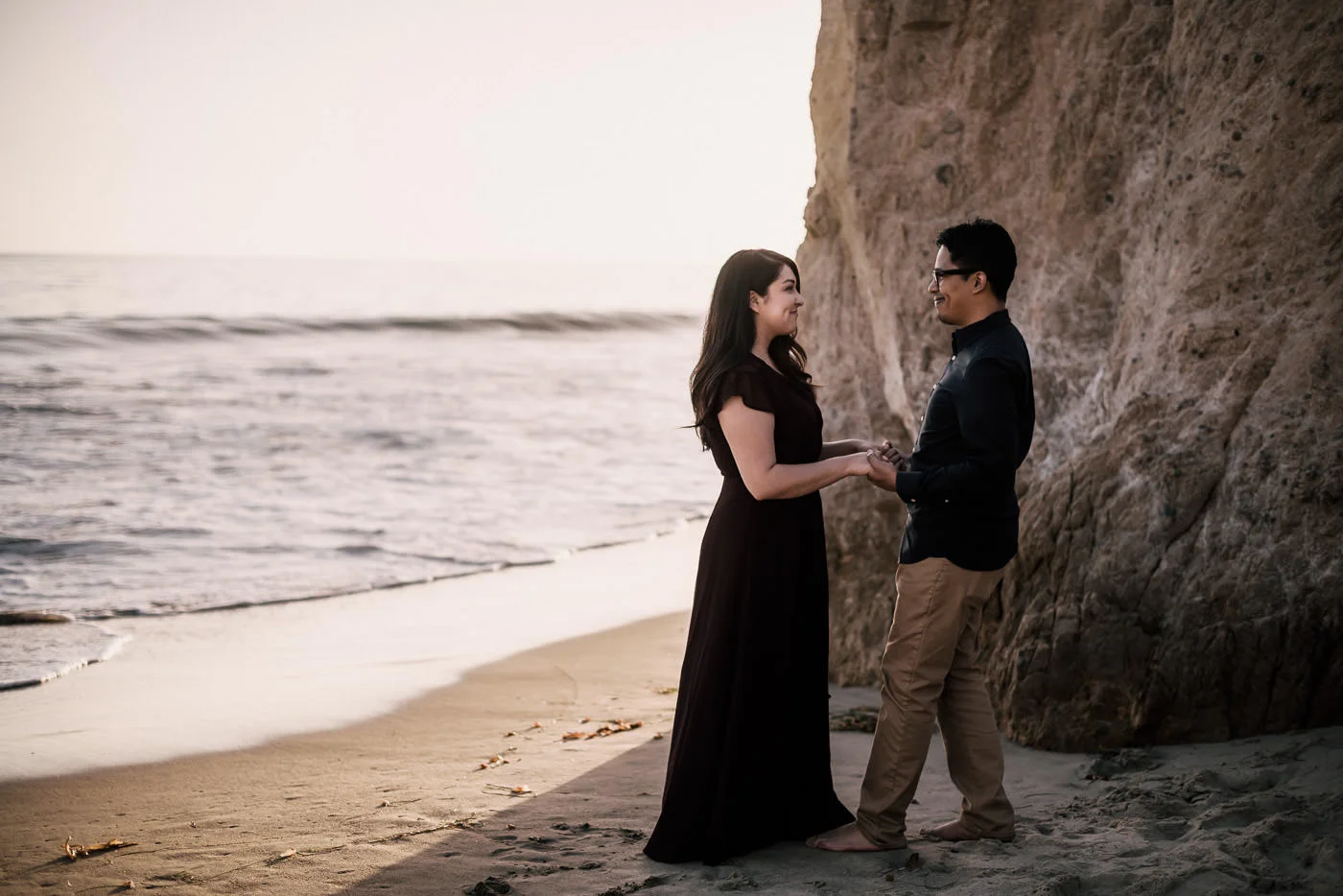 Pair of lovers holds hands on the beach and enjoys the sand in their toes during their El Matador beach Engagement.