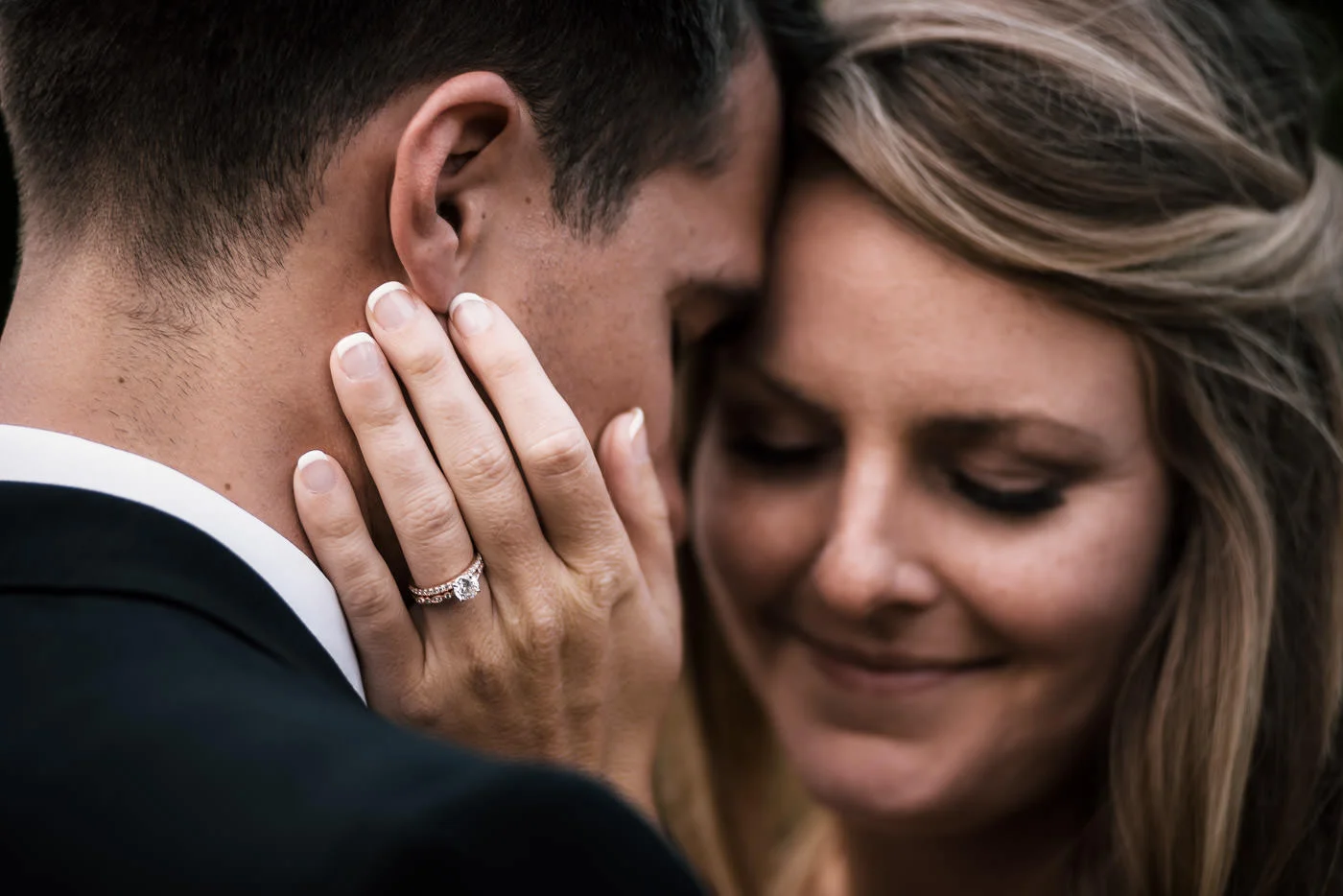 Bride places her hand tenderly on her husbands face and shows off her rings as the couple snuggles in close.