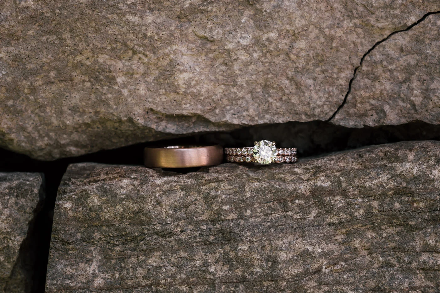 Wedding rings sit beside eachother in the narrow gap between stones on a rock wall.