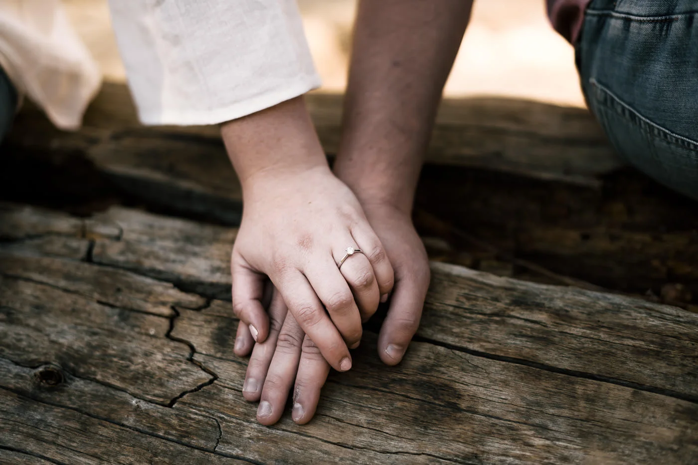 Love birds hold hands on a log to show off the beautiful engagement ring.