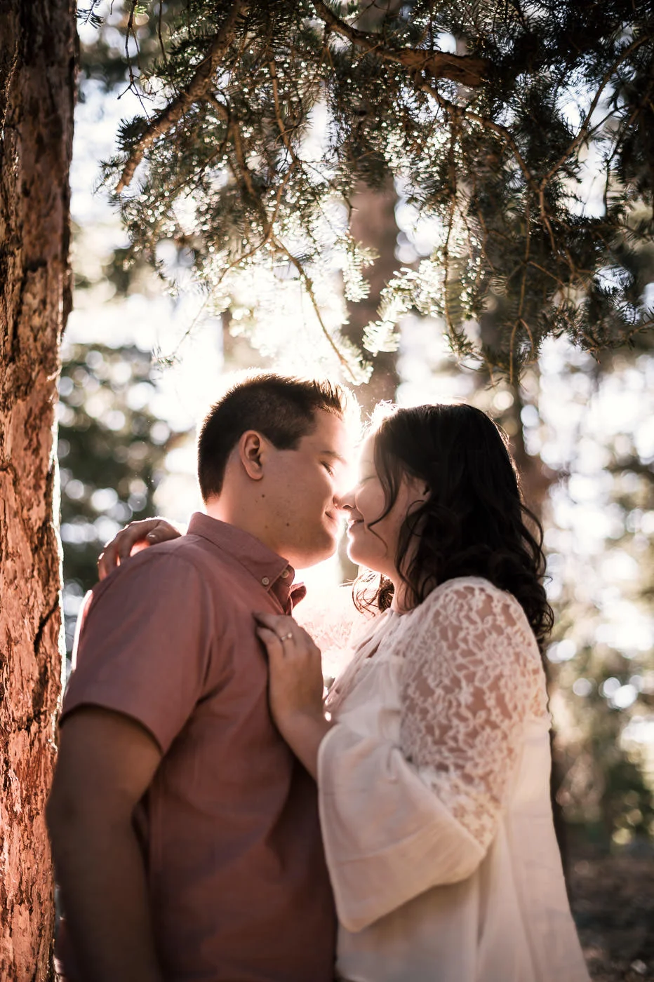 The bright light of sunset filters through the trees behind this engaged couple.