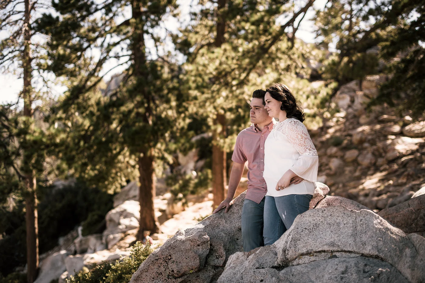 Lovers stand atop a mountain and look off into the distance during their engagement shoot.