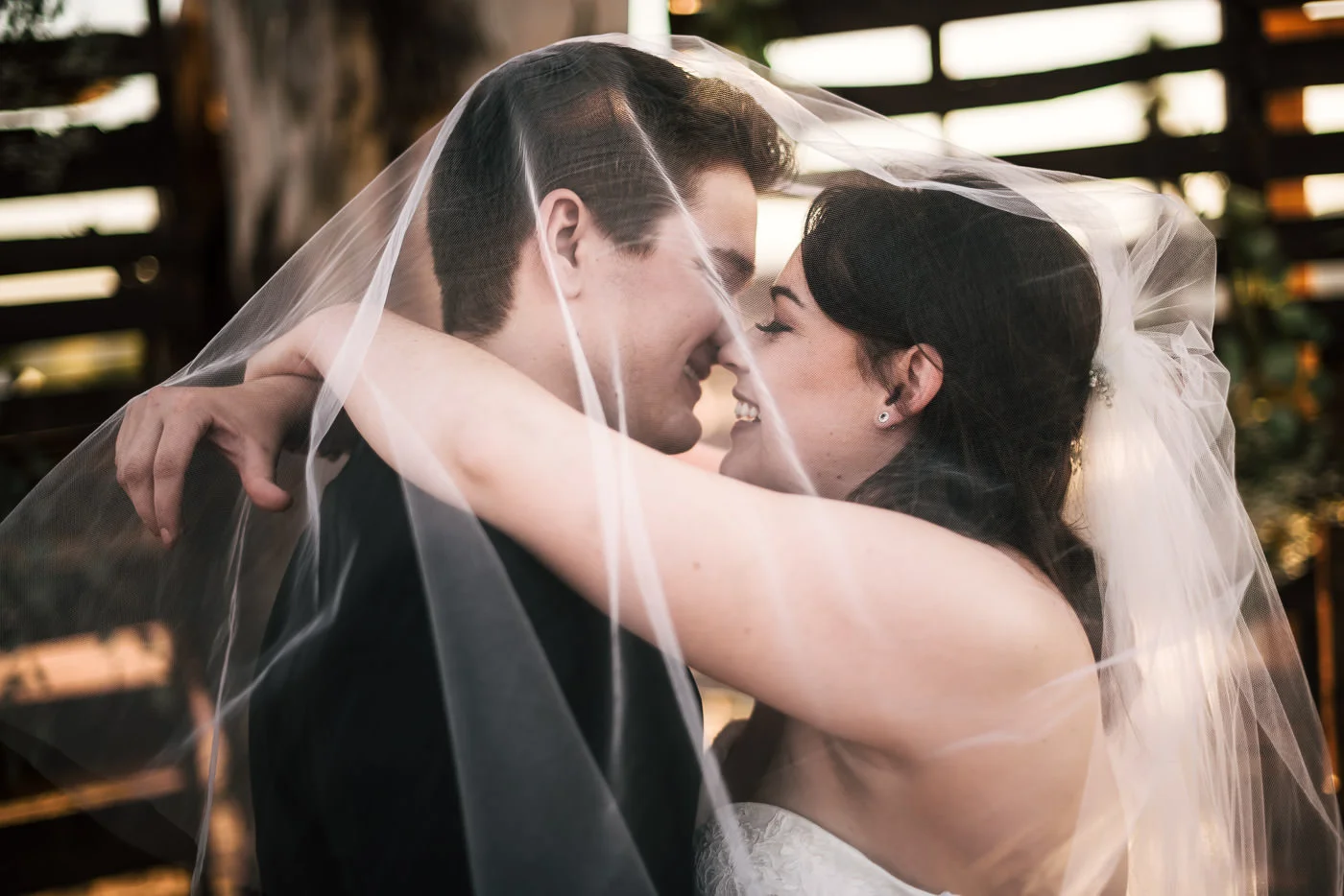 Bride and groom kiss under the wedding veil in front of a pallet wall at their Temecula wedding.