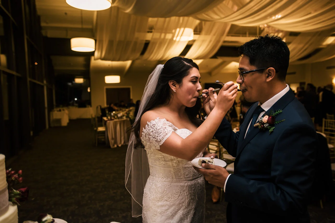 Bride and groom feed each other cake at their reception.