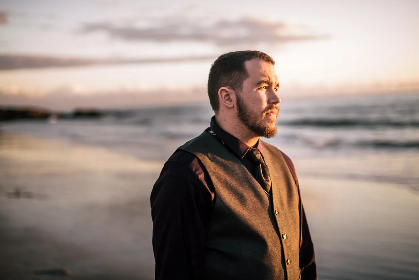 Groom gazes off at the setting sun after a romantic wedding.