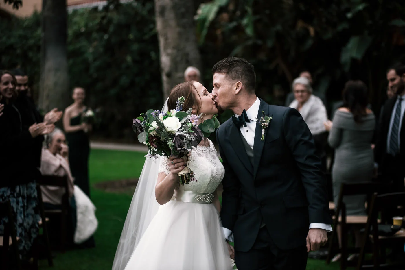 Newlywed couple stops for a kiss as they leave their wedding ceremony.
