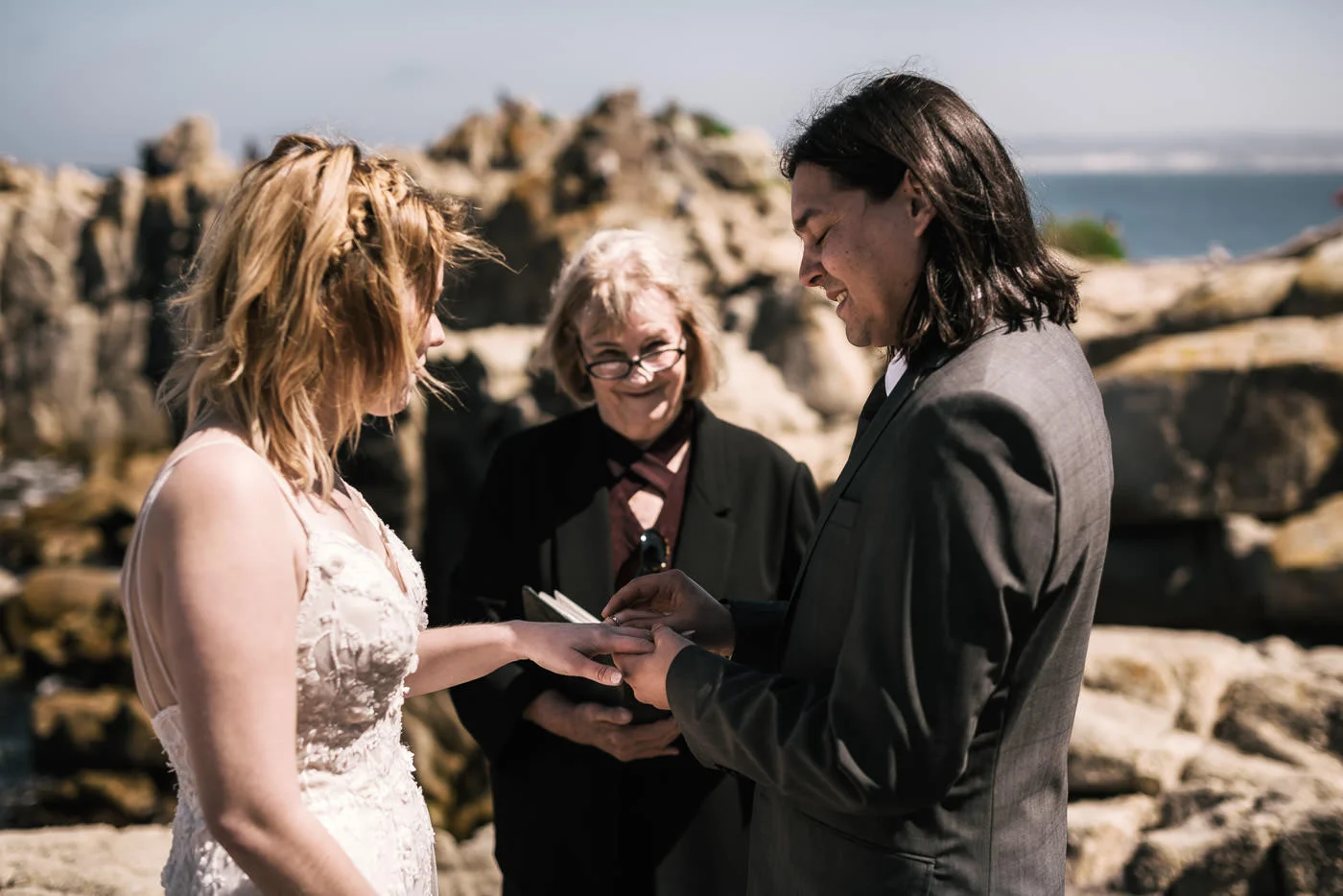 Groom places wedding ring on brides finger during marriage ceremony.