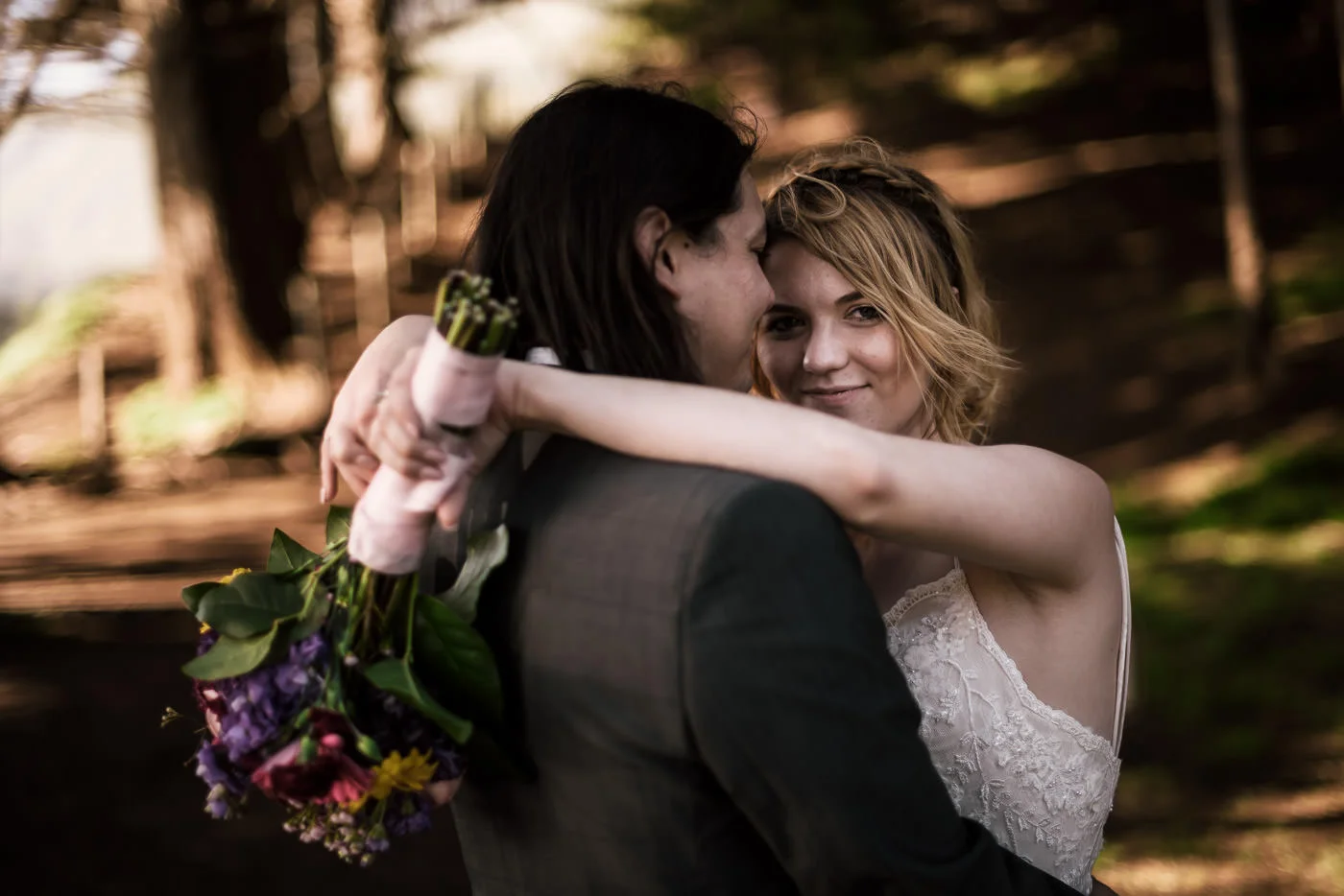 Bride smiles at the camera as she wraps her arms around her husband after eloping to Big Sur.