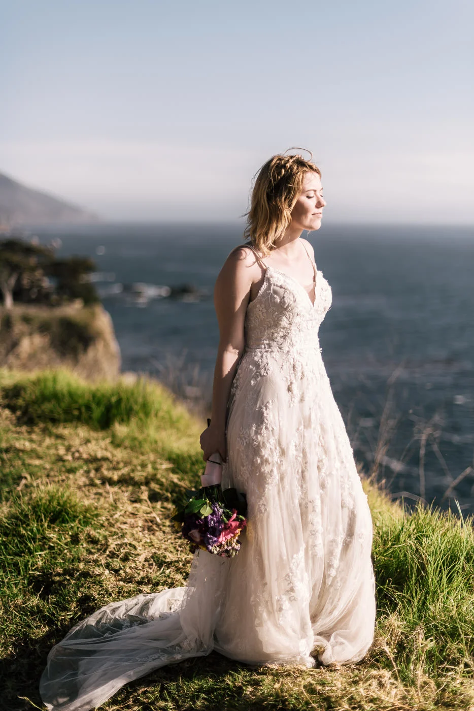 Bride stands on the cliffs of California's unforgettable coastline as the sun sets.