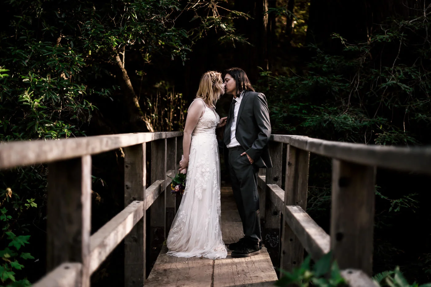 Tender kiss on an old wooden bridge spanning a creek after eloping in Monteray.