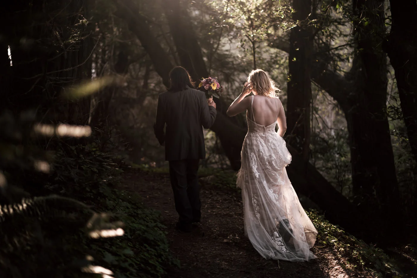 Newly married pair wnaders through the woods at sunset.
