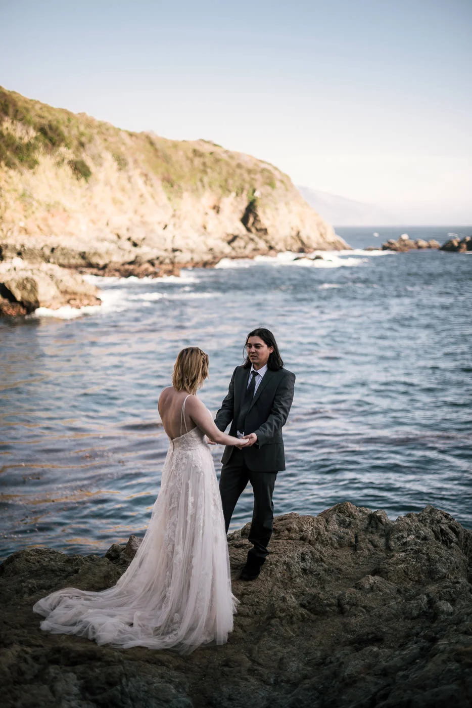 Couple in love holds hands besides the pacific ocean at sunset.