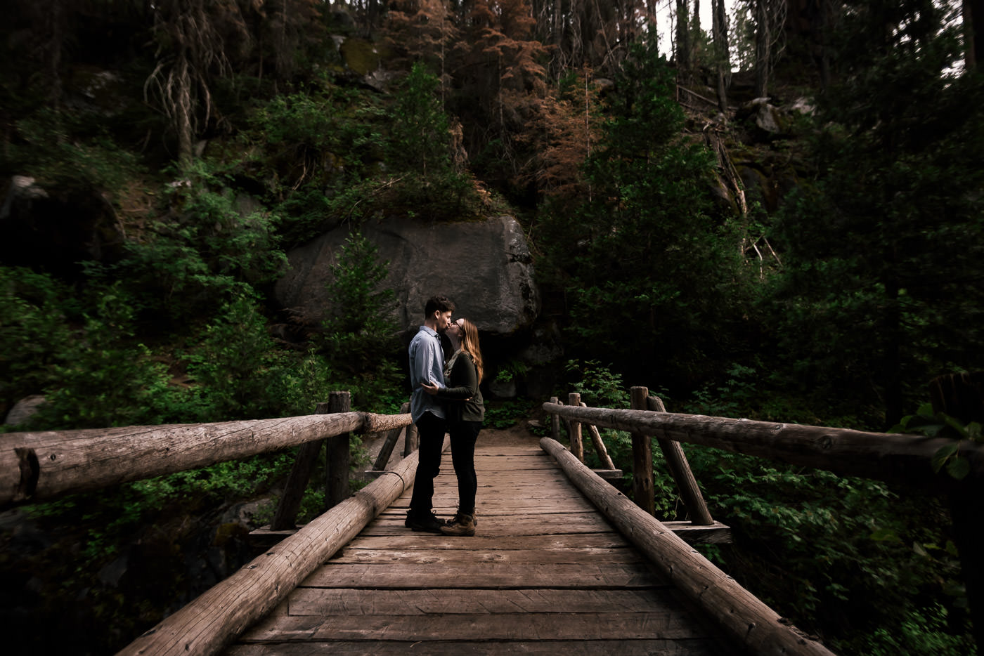 romantic kiss between a couple on an old wooden bridge during their intimate engagement session in seqouia national park