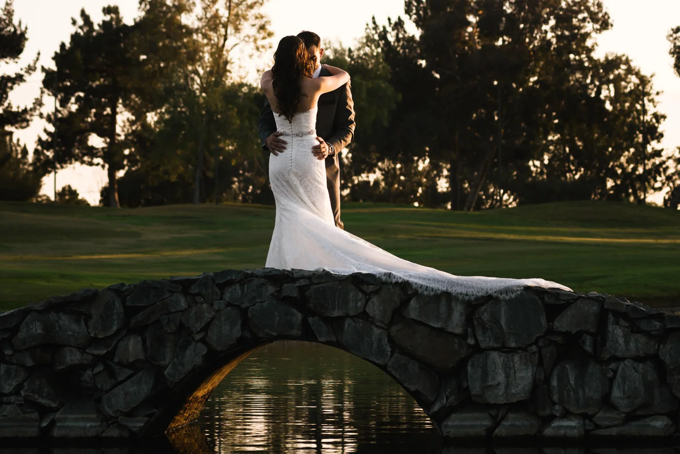Newlyweds stand atop a beautiful stone bridge over a pond at the Alta Vista Country Club in Placentia.