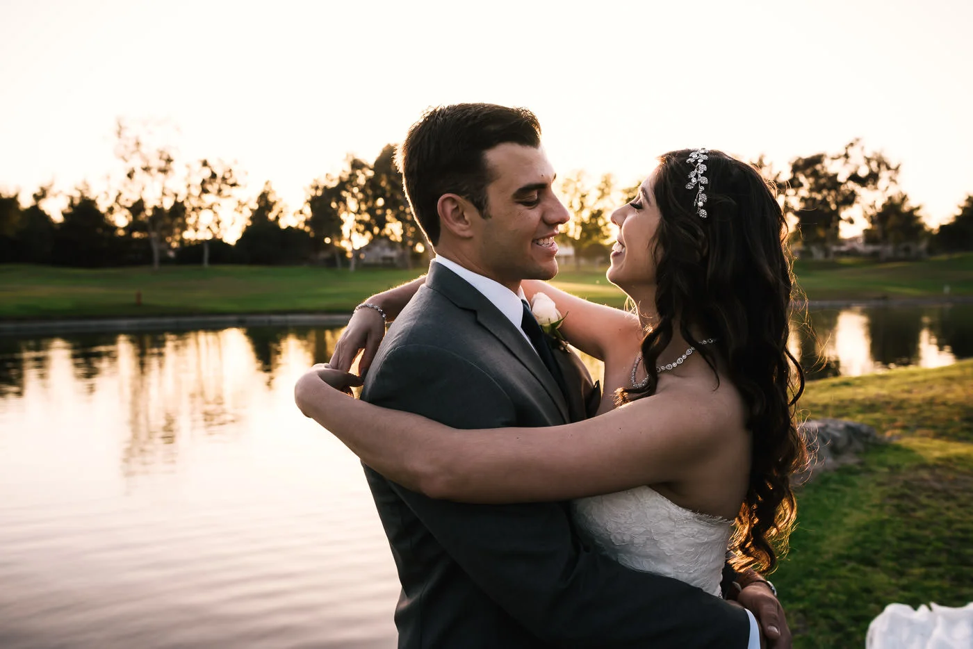 Couple holds each other close as the sun sets on the pond behind them.