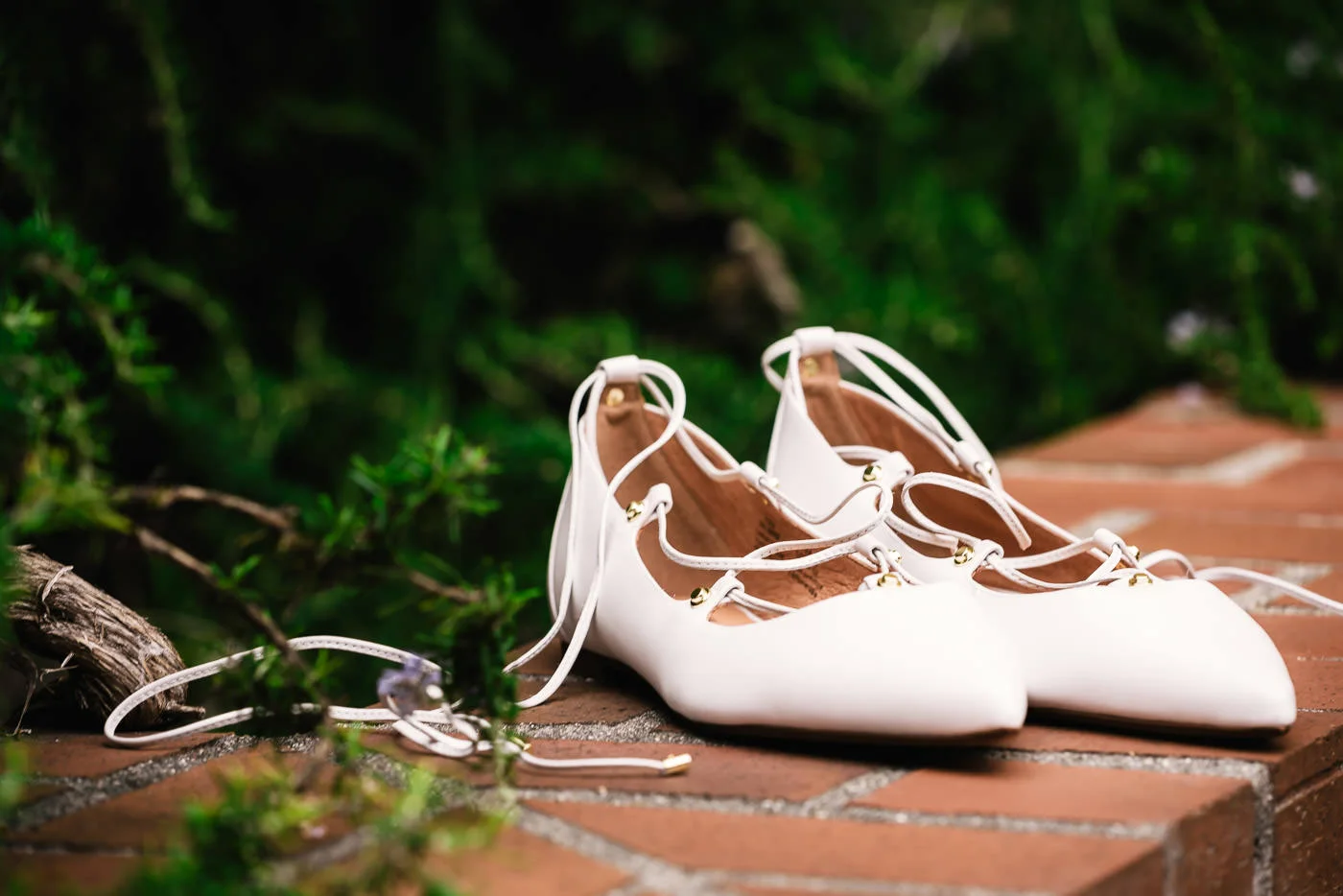 Bride's white shoes sit on a brick wall.