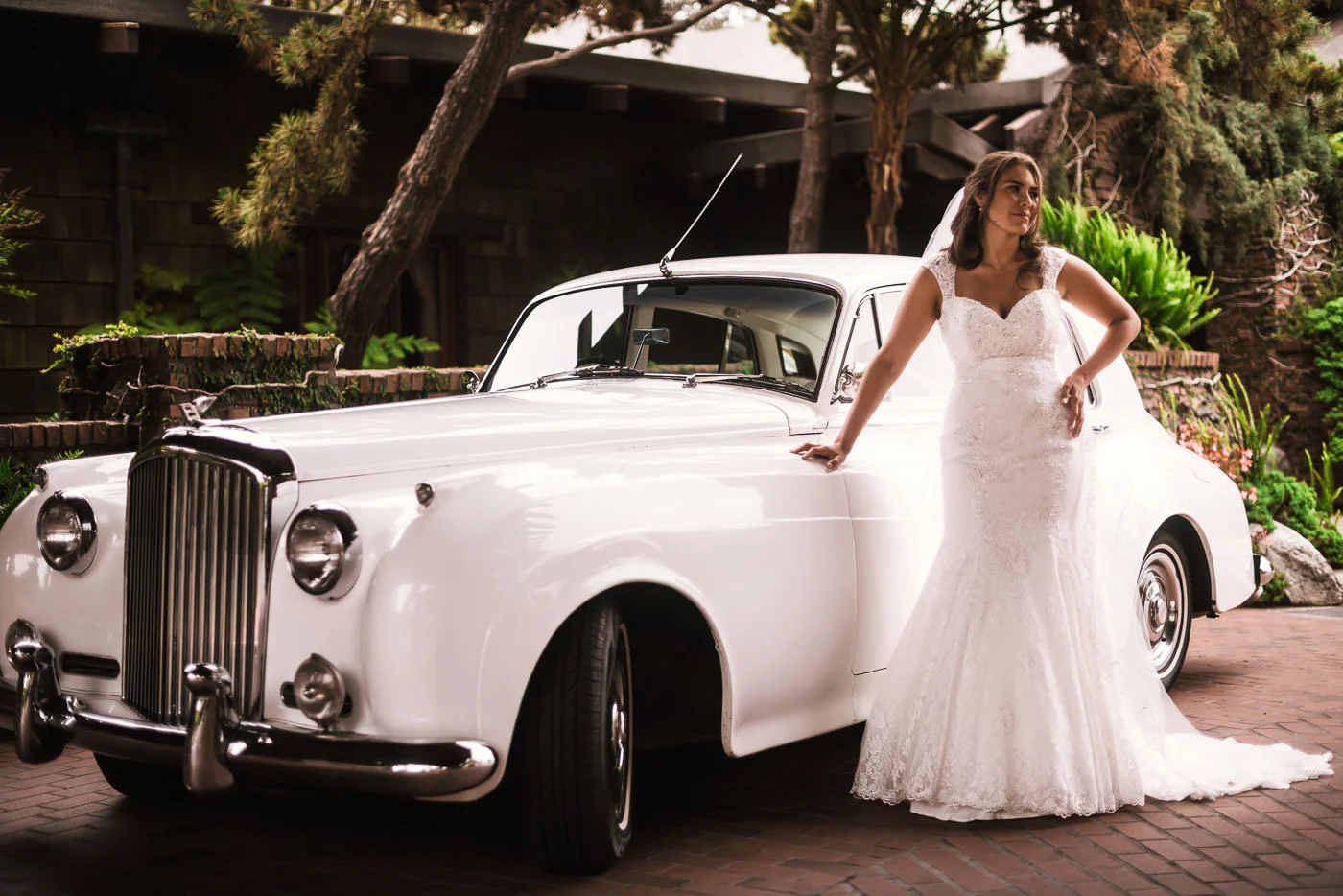 Beautiful bride poses with a classic Rolls Royce before taking it to her wedding.