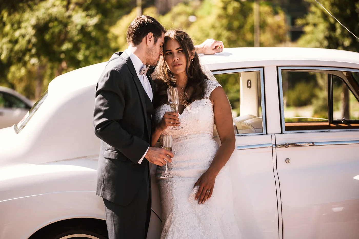 Couple toasts their new marriage with glasses of champagne in front of a classic Rolls Royce.
