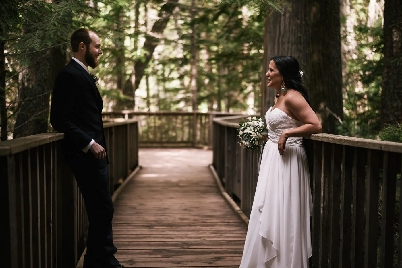 Bride and groom lean back for a casual photo among the cedars.