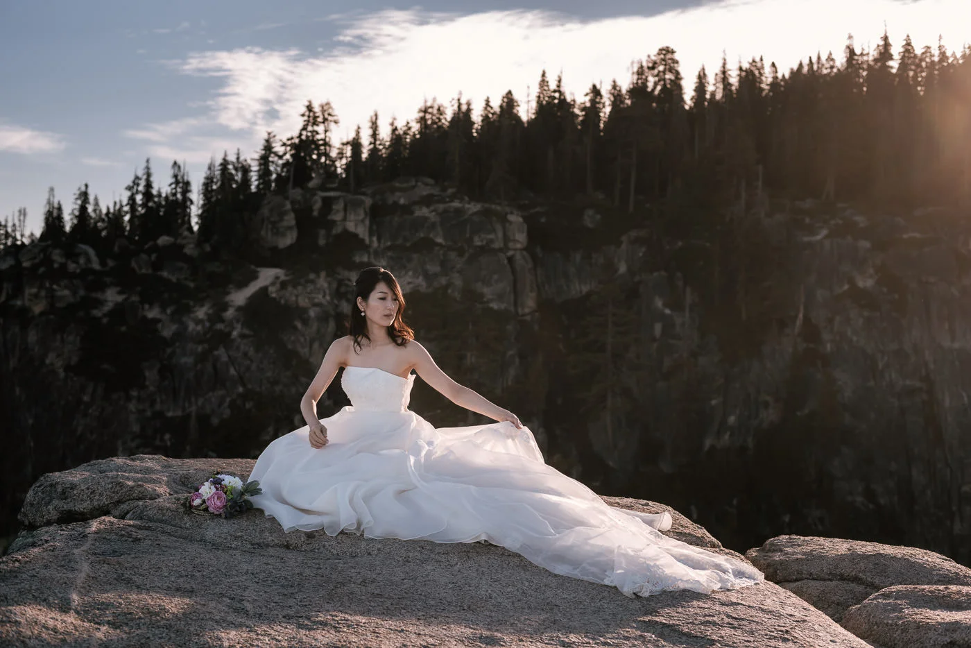 Bride fixes dress for a stunning portrait at sunrise atop a mountain in the National Parks of California.