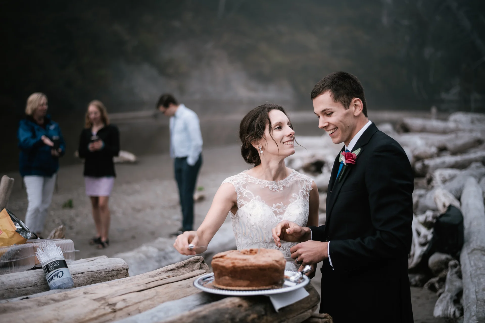 Couple prepares to cut their wedding cake on a driftwood table at Ruby Beach.
