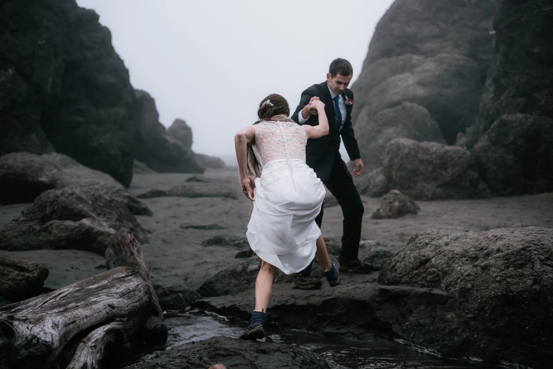 Adventurous bride hikes up her wedding dress to cross a creek at Ruby Beach.