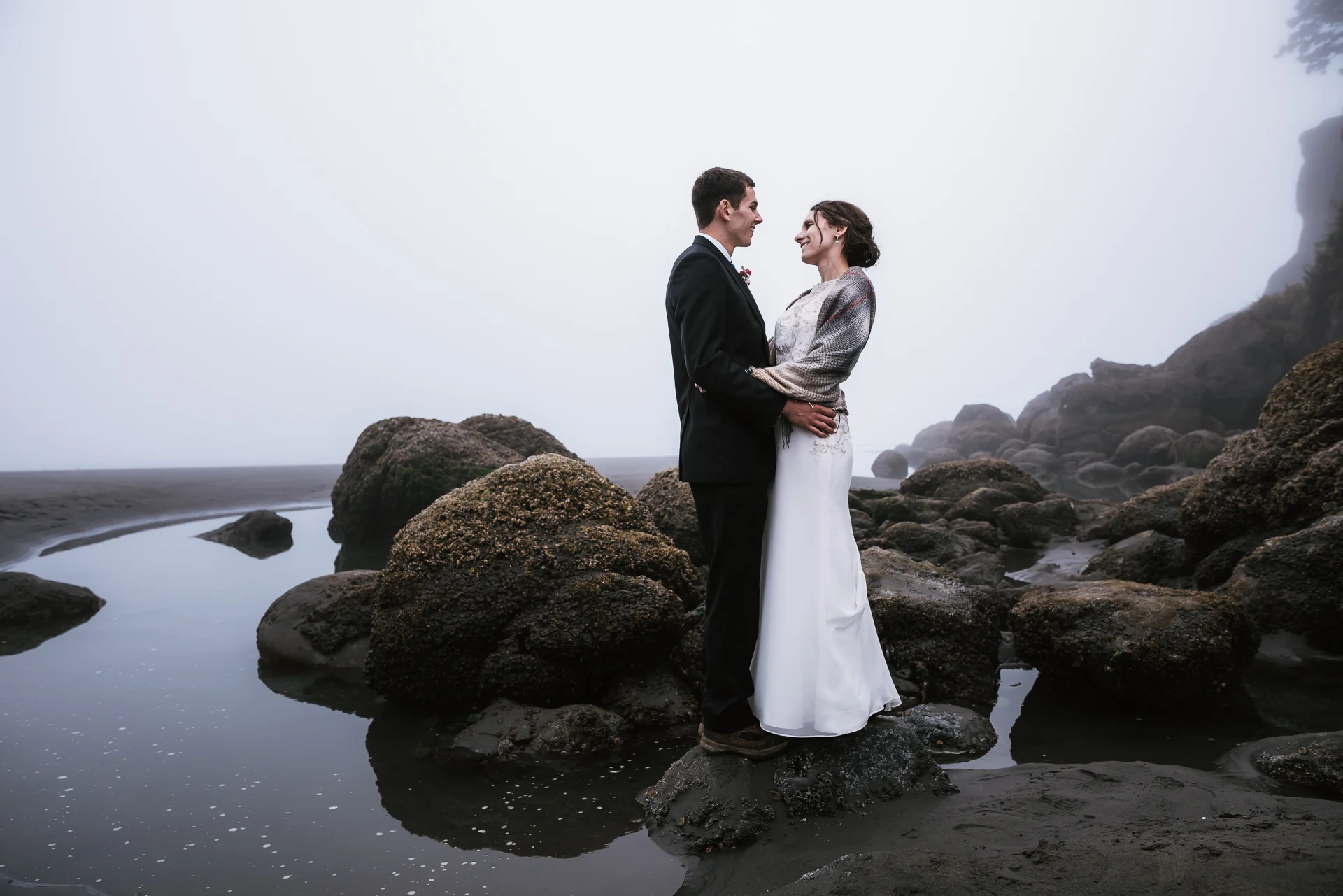 Newly married couple poses next to a tide pool in the foggy coastline of Washington.