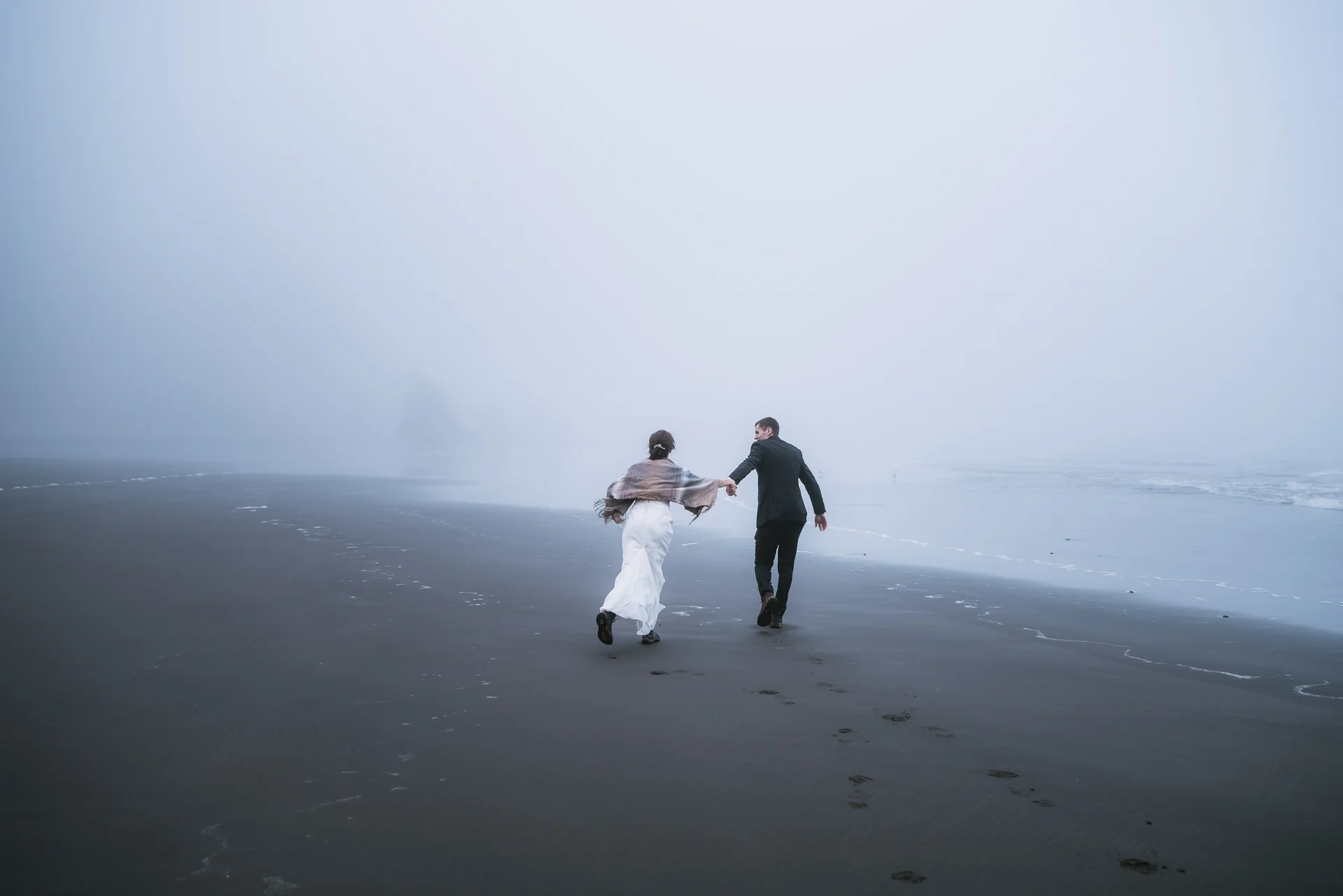 Newlyweds run down the black sand of Ruby Beach in Washington.