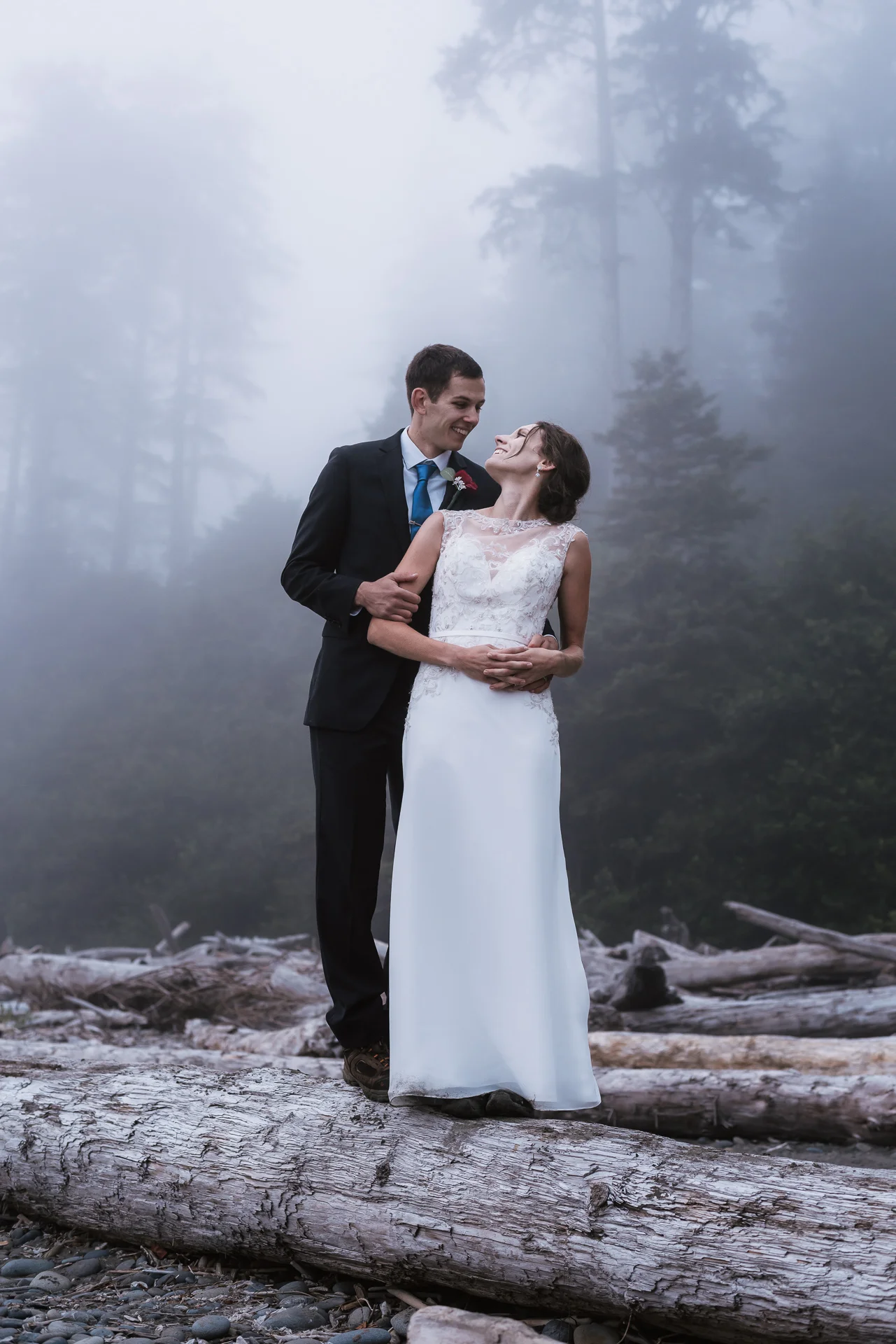 Couple stands on an old piece of driftwood and stares deeply into each other's eyes.
