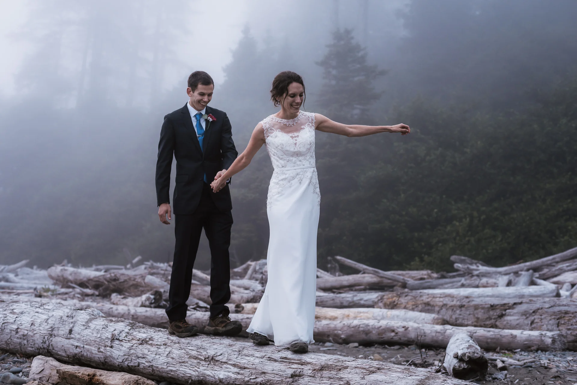 Adventurous couple balances on a log in their formal wedding attire.