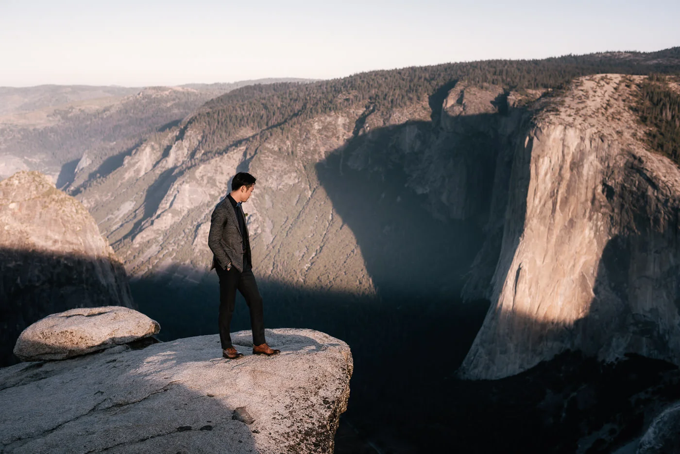 Eloping groom stands on the granite cliff and looks out over the beautiful landscape.