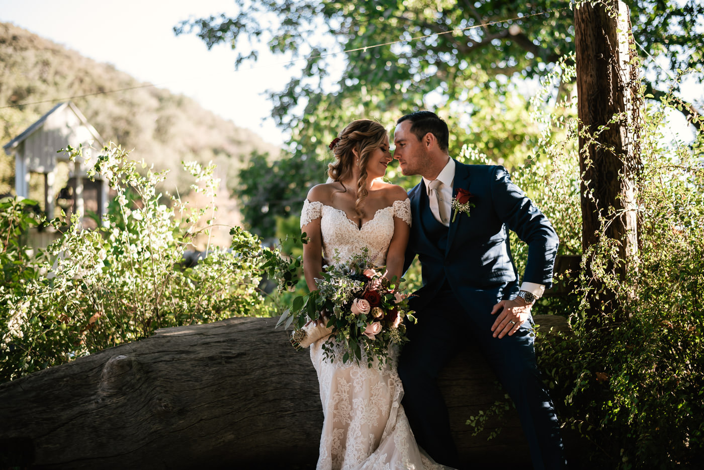 Married couple sits on a log and stares into each other's eyes.