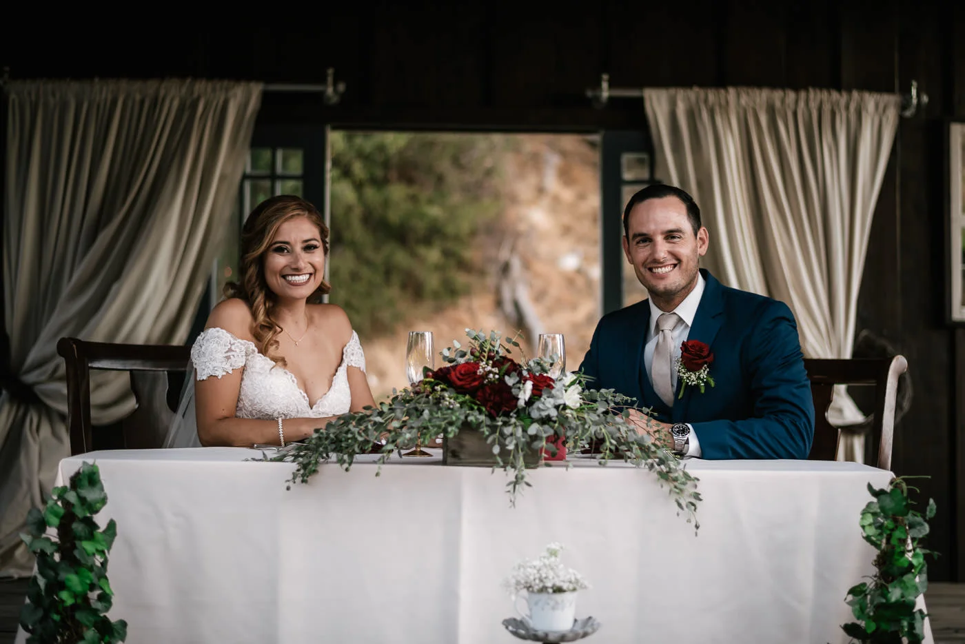 Bride and groom take a seat at their sweetheart table and prepare to eat at their reception.