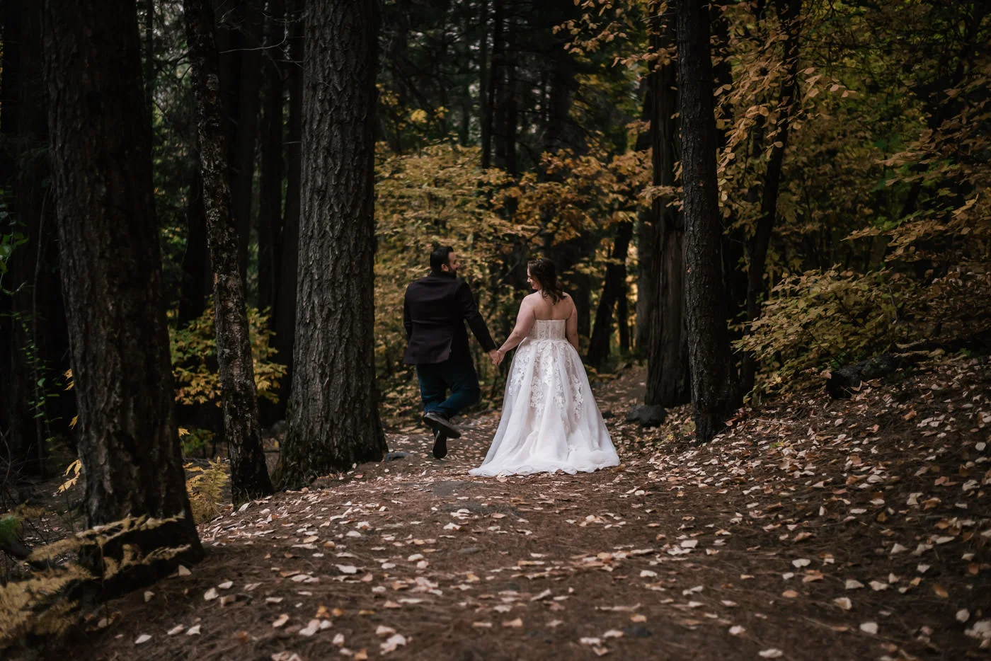 Groom jumps and clicks his heels together with joy as he walks with his new bride through the forest, captured by their elopement photographer.