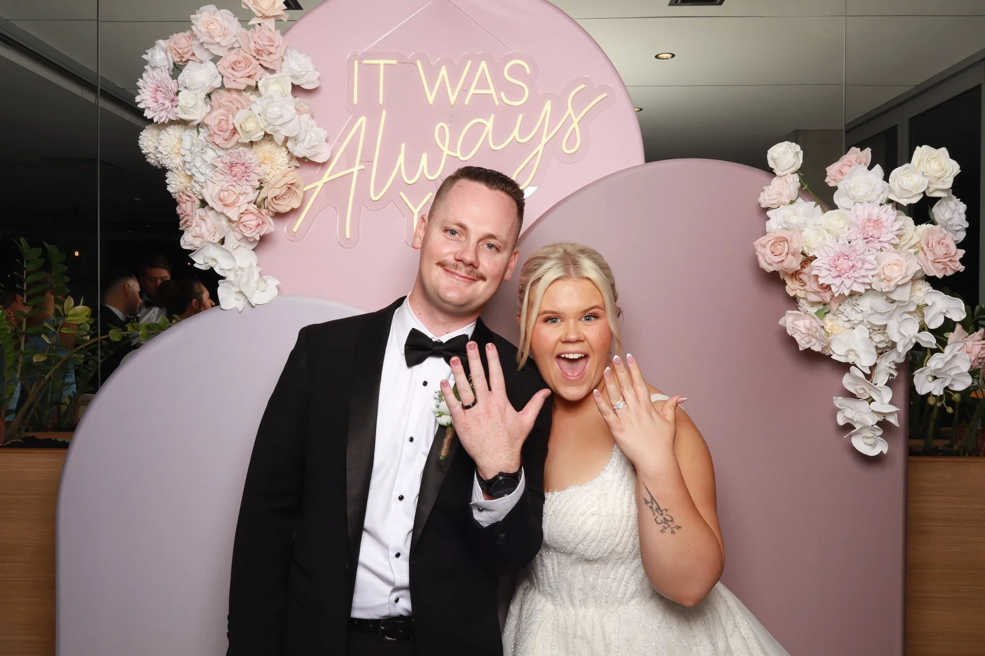 Wedding couple celebrating in the photo booth with the Blush Horizon layered arch backdrop and floral styling.