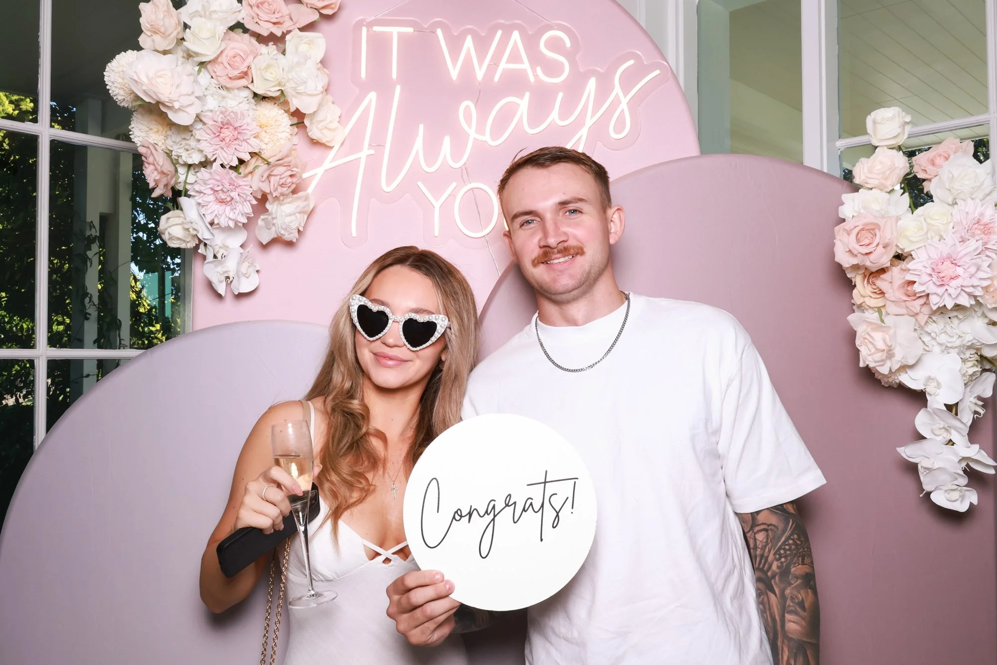 Wedding guests posing with a Congrats sign in front of the Blush Horizon pink arch photo booth backdrop.