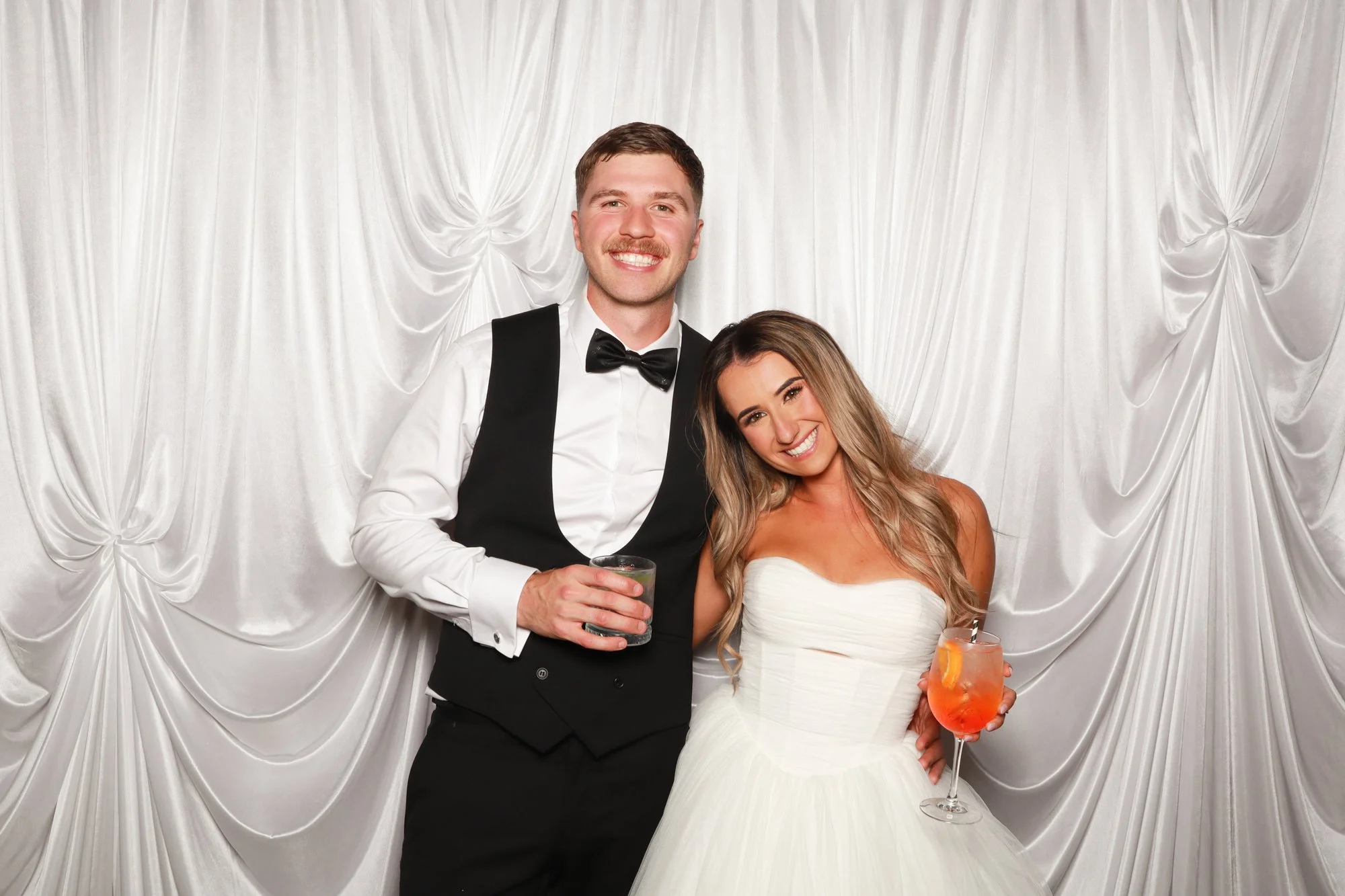 Wedding couple posing in front of the luminous gathered folds of the Ivory Silk Drape photo booth backdrop.