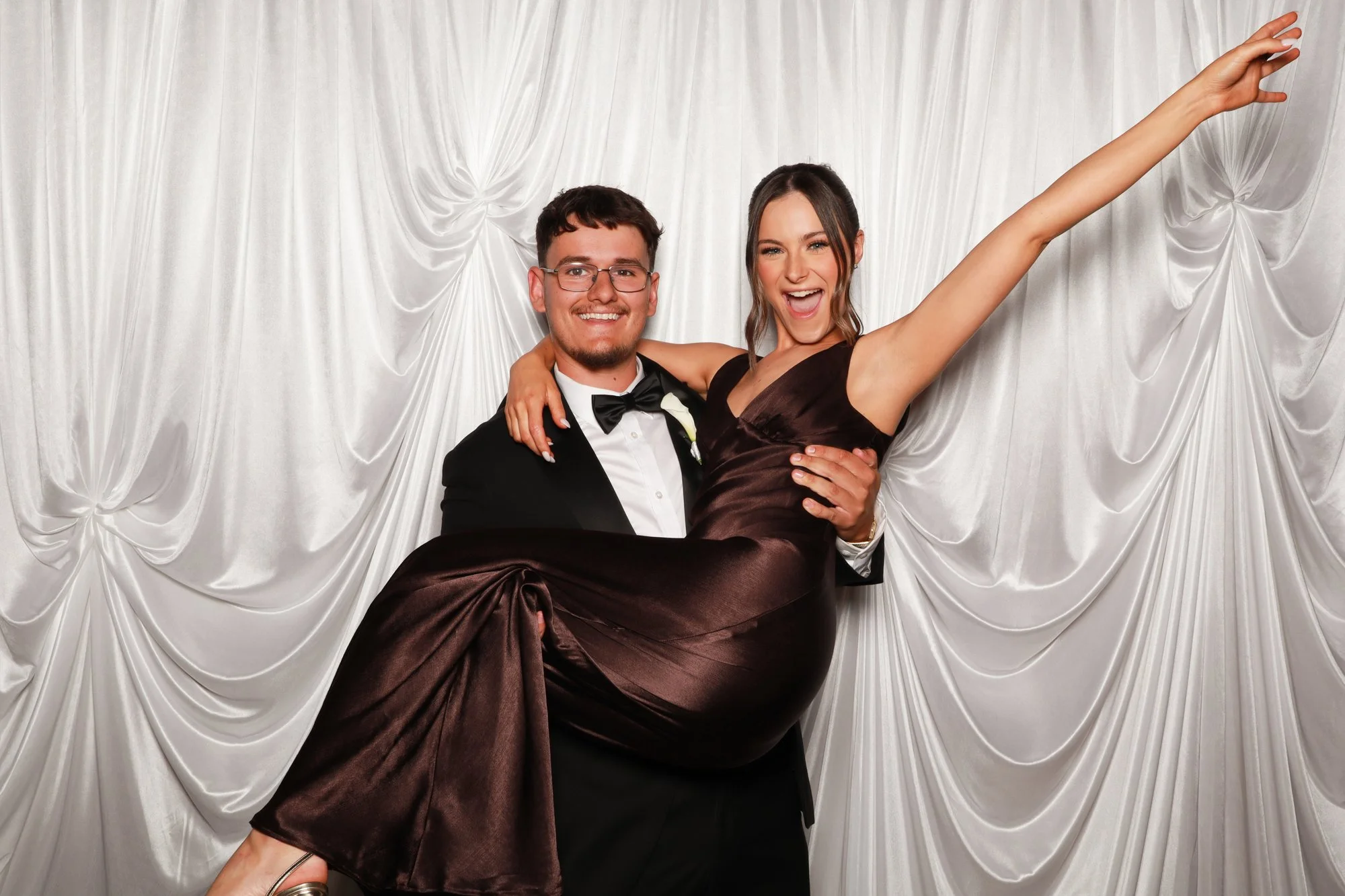 Wedding guests celebrating against the soft cascading folds of an ivory silk draped photo booth backdrop.