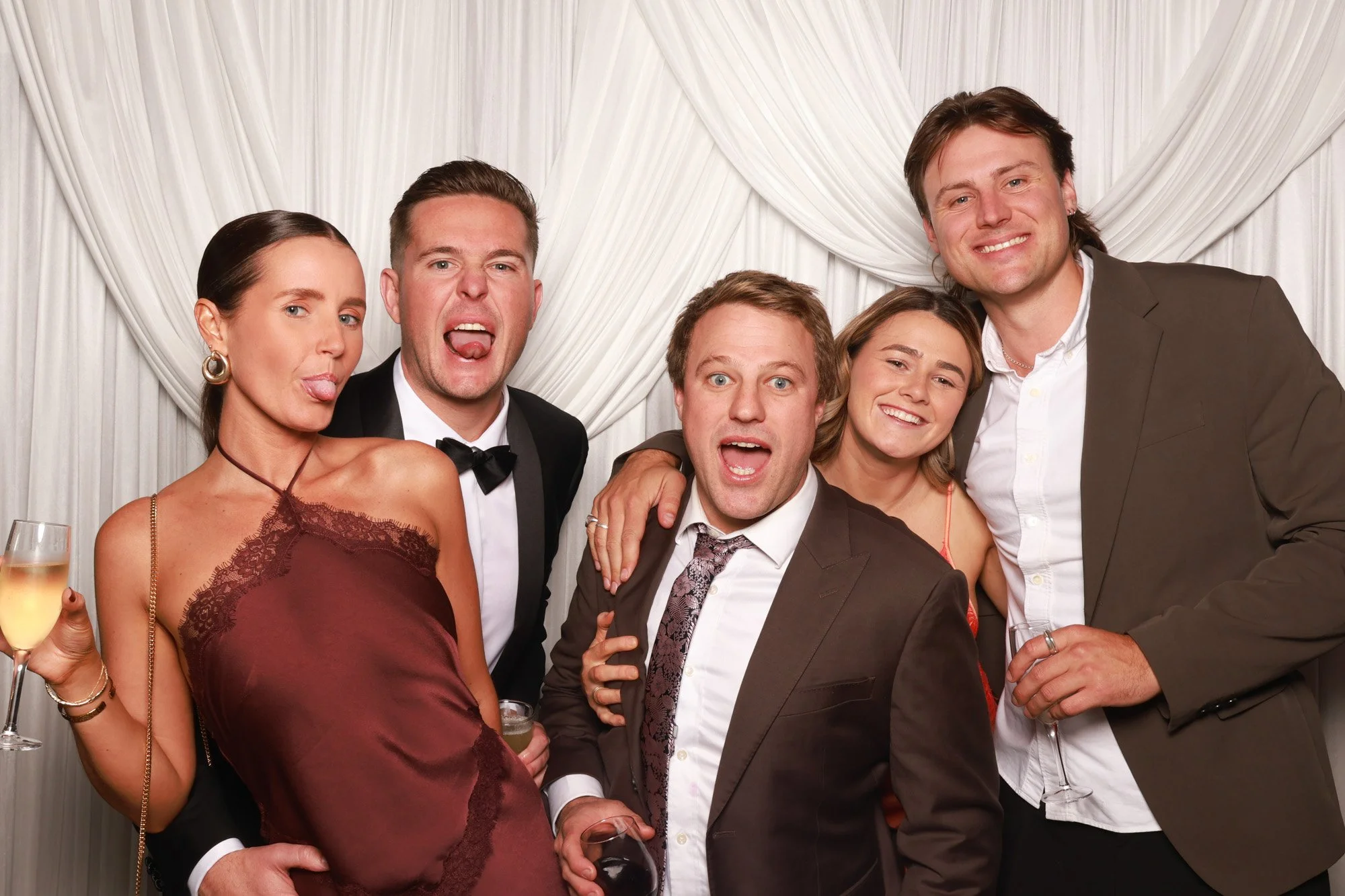 Guests celebrating in front of an elegant ivory draped photo booth backdrop with soft dimensional folds.