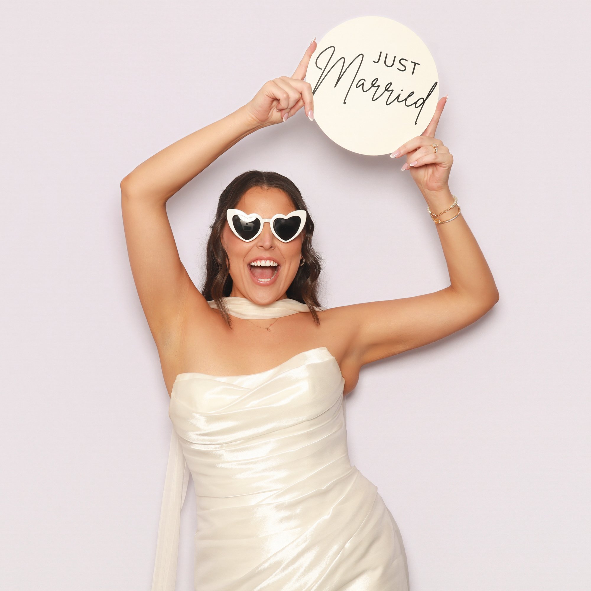 Bride wearing heart-shaped sunglasses and holding a Just Married sign in a Photo Corner photo booth.