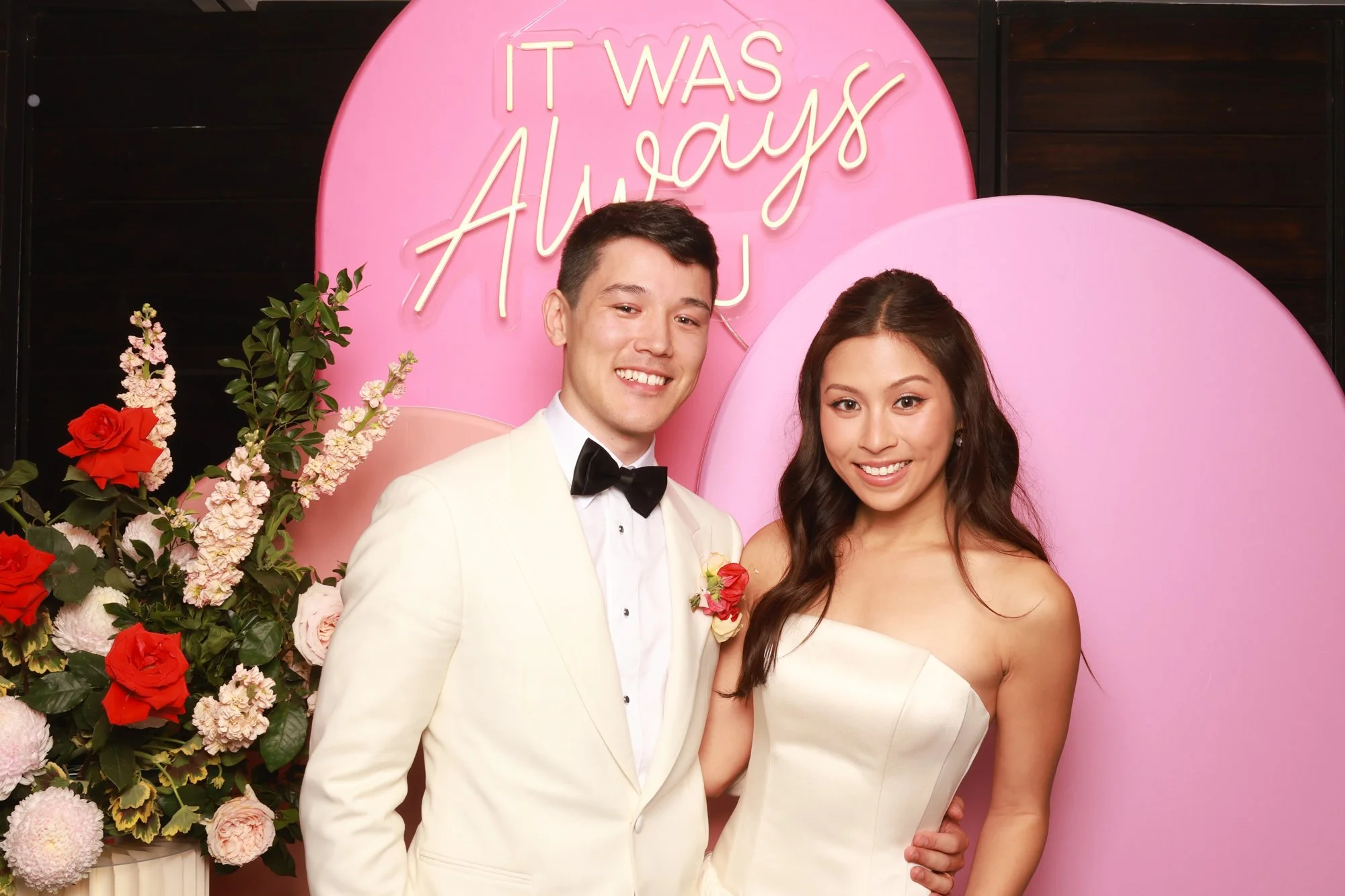 Wedding couple posing against layered tonal pink arches with a glowing neon sign.